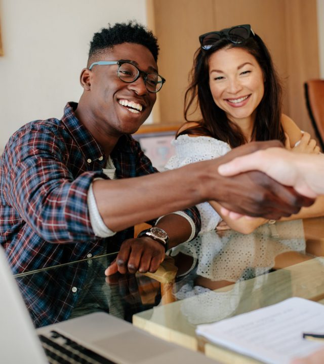 Happy property owners shaking hands with real estate broker after a deal. Young couple handshaking real estate agent after signing contract.